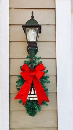 a christmas wreath hanging on the side of a house next to a lamp post with a clock