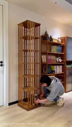 a man kneeling down next to a tall wooden bookcase in a room with bookshelves