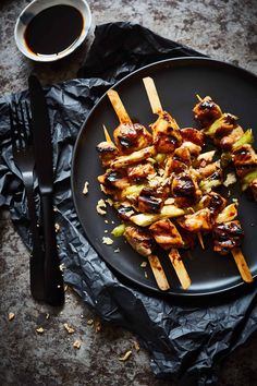 chicken and vegetable skewers on a black plate next to a cup of coffee