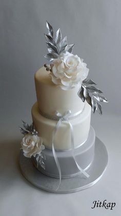 a three tiered wedding cake with white flowers on top and silver leaves around the edges