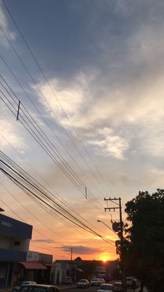 the sun is setting behind power lines and cars are parked on the side of the road