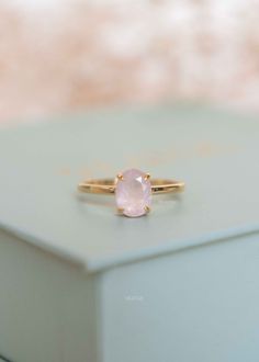 a pink stone ring sitting on top of a white box with gold trimmings