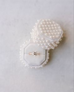 two pearls and a ring on top of a white cloth covered box with a diamond in the middle