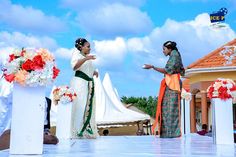 two women are standing in front of some white and orange flowers on a stage with an audience