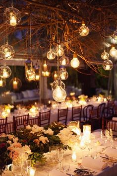 a table topped with lots of white flowers and lit up candles in front of a tree