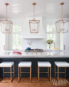 a kitchen island with four stools in front of it and three lights hanging from the ceiling