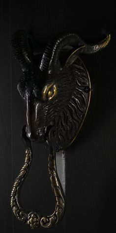 a black goat head mounted to the side of a door with an ornate brass handle