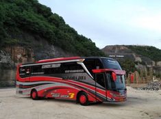 a red and black bus parked on the side of a road next to a mountain