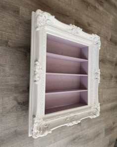 an ornate white shelf with pink shelves in the middle on a wooden wall behind it