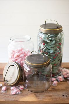 three glass jars filled with candy canes sitting on top of a wooden table next to other