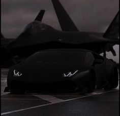 a black sports car sitting on top of an airport tarmac next to a fighter jet