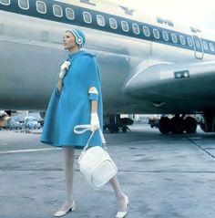 a woman in a blue coat is walking towards an airplane