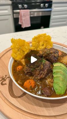 a white bowl filled with meat and vegetables on top of a wooden cutting board next to an oven