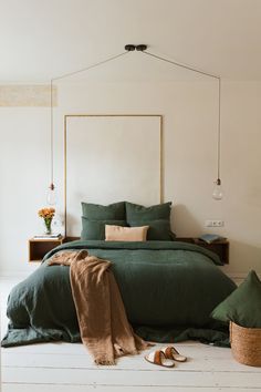 a bed with green linens and pillows in a white room next to a plant