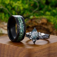 two wedding rings sitting on top of a wooden table next to another ring with green and white flowers