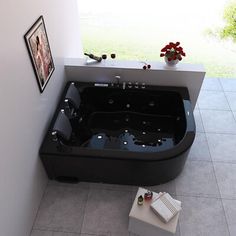 a black bath tub sitting on top of a tiled floor next to a window with flowers