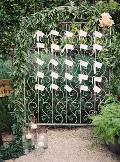 an iron gate with flowers and candles on it in the middle of a garden area