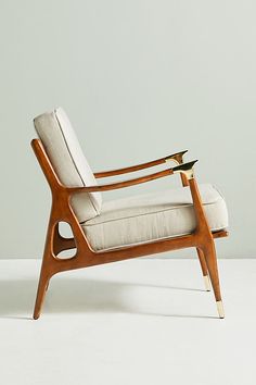 a white chair with a wooden frame and arm rests against a gray wall in an empty room