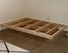 an unfinished bed frame sitting on top of a hard wood floor next to a white wall