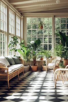 a sun room filled with lots of plants and wicker furniture in front of large windows