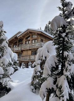 snow covered pine trees in front of a large wooden building with balconies and balconies on the second floor