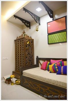 a bed sitting next to a wooden cabinet with colorful pillows on it's sides