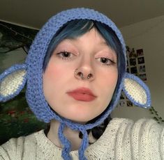 a woman with blue hair wearing a crocheted hat and nose ring is looking at the camera