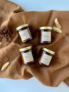 three jars of honey sitting on top of a brown cloth next to a pine cone