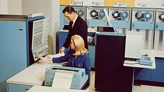 two people are working in an old computer room with many machines and computers on the walls