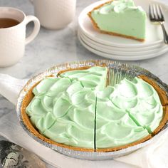 there is a pie with green frosting in the pan on the table next to plates and cups