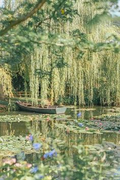 a small boat floating on top of a lake surrounded by lily pads and willow trees