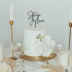 a white wedding cake sitting on top of a table next to wine glasses and candles