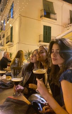 four women sitting at a table with wine glasses in their hands and one woman holding a drink