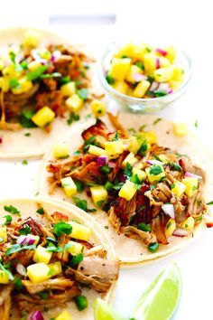 three pork tacos with pineapple salsa and lime wedges on the side,