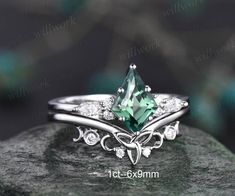 an engagement ring with a green stone surrounded by white diamonds on top of a rock