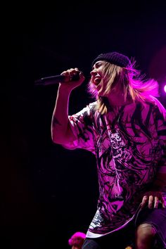 a male in a black and purple shirt singing into a microphone