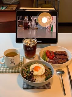 a table topped with bowls of food next to a laptop computer and cup of coffee