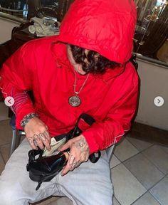 a man in a red hoodie is sitting on a chair with his shoes and money