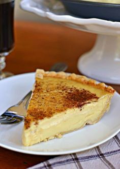 a piece of pie on a white plate with a fork and cake dish in the background