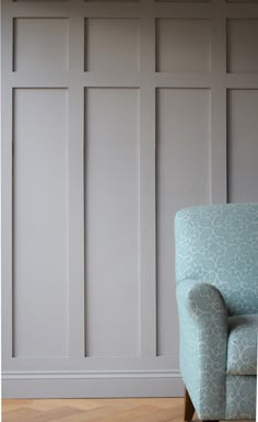 a blue chair sitting in front of a wall with white paneling on the walls