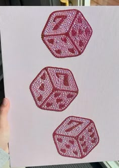 three pink dices are on a white piece of paper that has been embroidered onto it