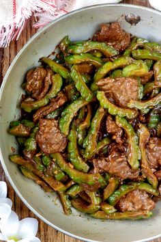 a bowl filled with beef and peppers on top of a wooden table next to flowers