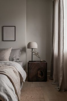 a bed sitting next to a window with curtains on both sides and a lamp on top of it