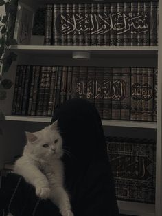 a white cat sitting on top of a person's lap in front of bookshelves