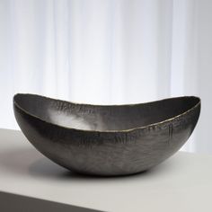 a large metal bowl sitting on top of a white table next to a curtained window