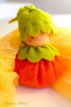 a small doll sitting on top of a yellow netted cloth bag and wearing a green hat