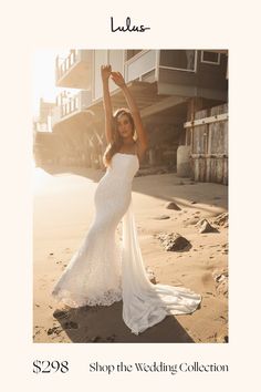 a woman in a white wedding dress on the beach with her arms up and hands behind her head