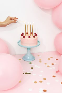 a person is lighting candles on a cake with pink and gold balloons in the background