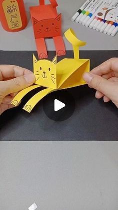 two hands are holding an origami cat and another hand is pointing at it