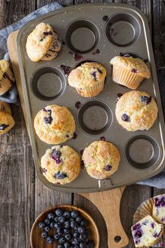 blueberry muffins in a muffin tin with fresh blueberries on the side